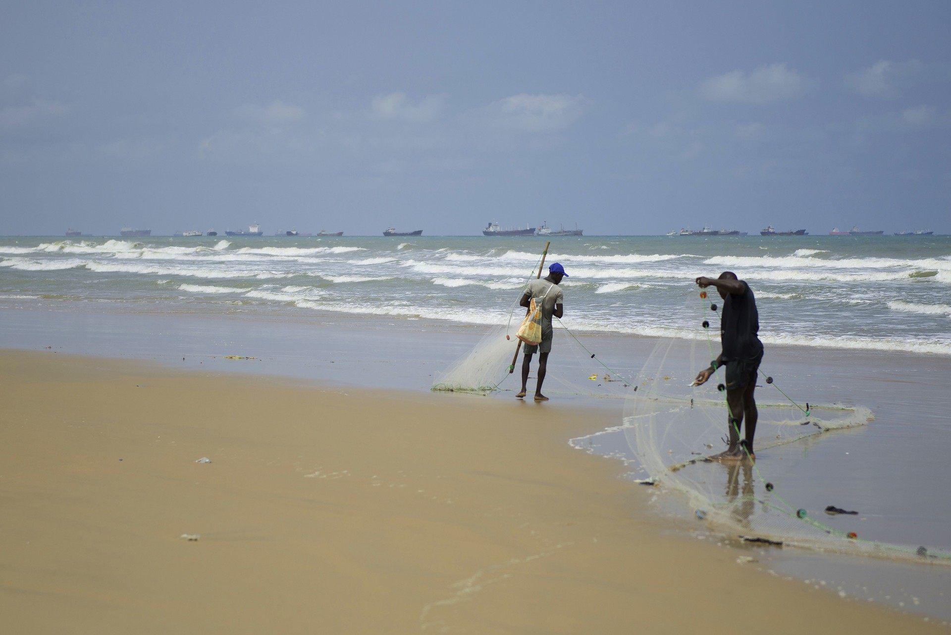 Fishermen catch fish with nets near africa cost . Big cargo ships and oil tankers in Lagos, Nigeria, Africa.